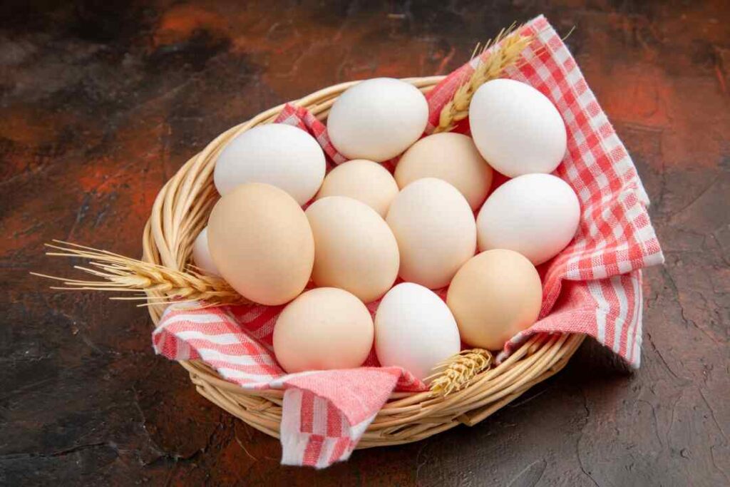 Front view white chicken eggs inside Basket with towel dark surface
